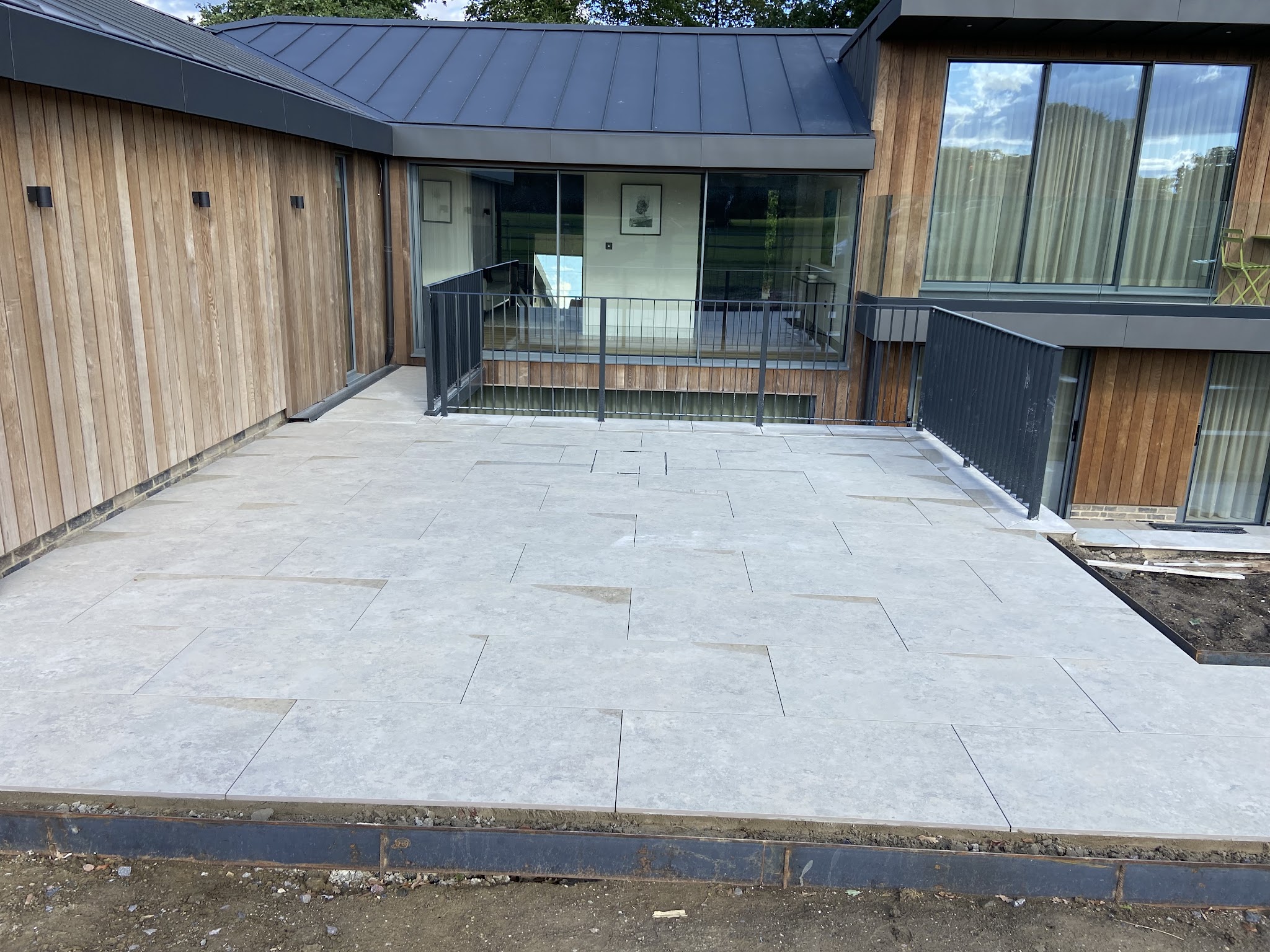Large pale porcelain patio laid in front of a modern timber-clad house