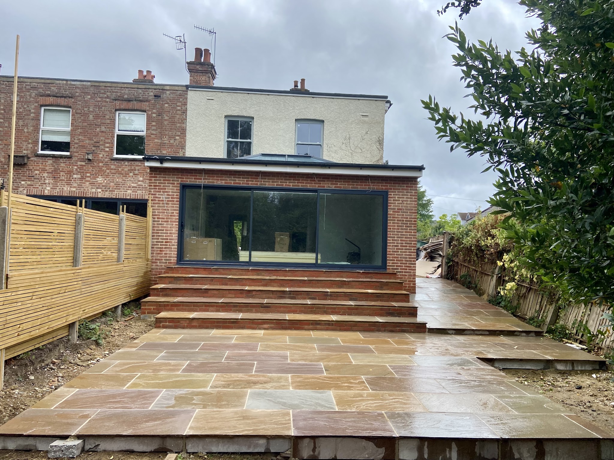 New patio and brick steps leading up to a rear extension with sliding doors