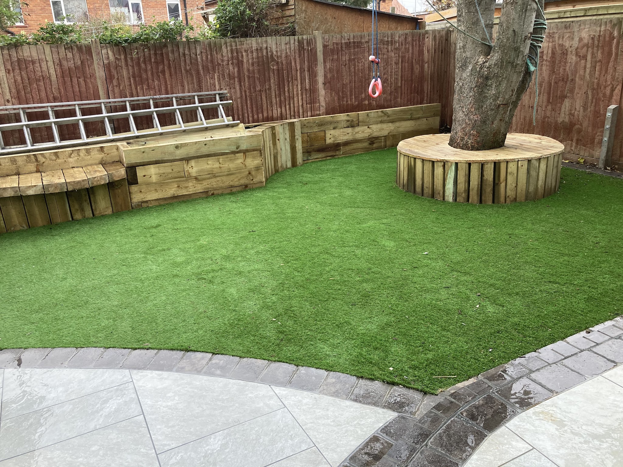 Sleeper walls, a round sleeper seat around a tree and an artificial lawn with a curved porcelain path