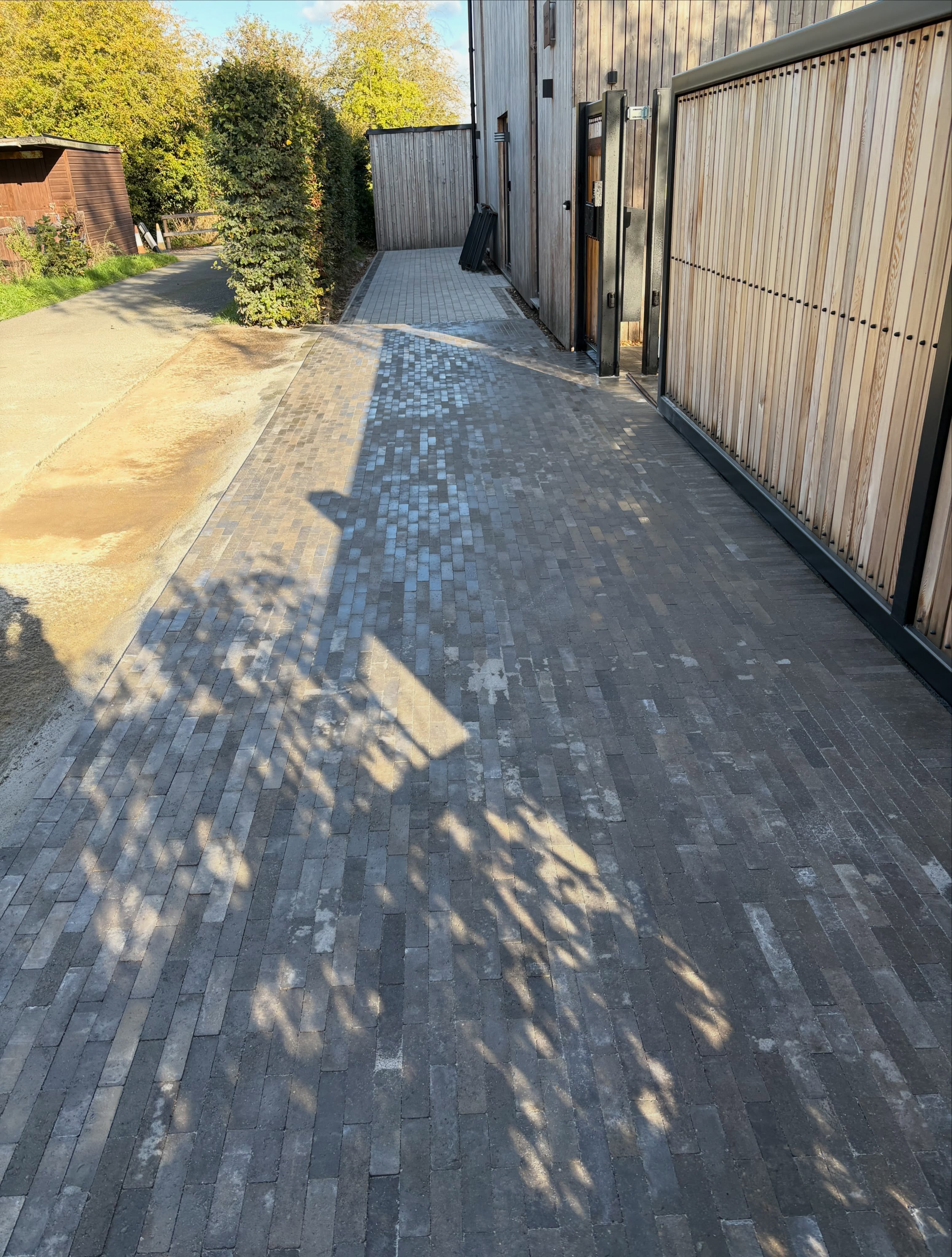 Long block paved driveway running beside tall timber gates